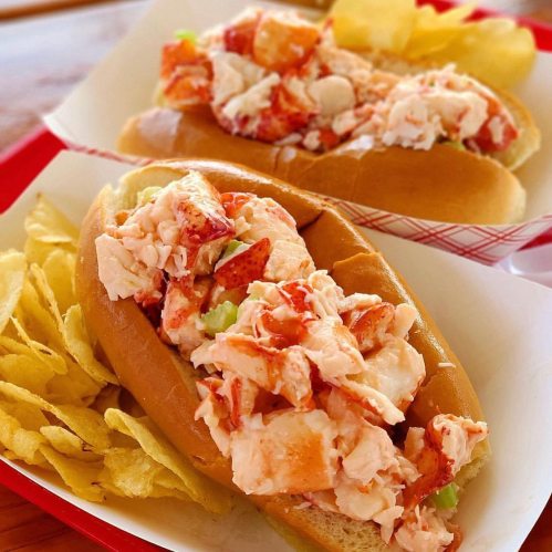 Two lobster rolls filled with lobster salad, served with a side of potato chips.