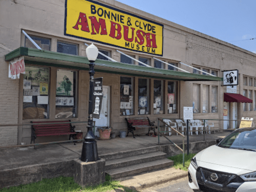 Exterior of the Bonnie and Clyde Ambush Museum, featuring a colorful sign and benches outside.