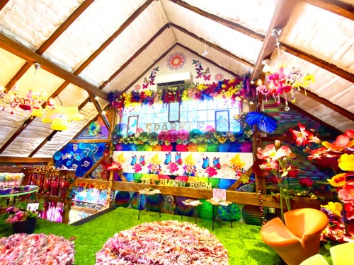 A vibrant, flower-themed interior with colorful decorations, greenery, and artistic displays in a cozy attic space.