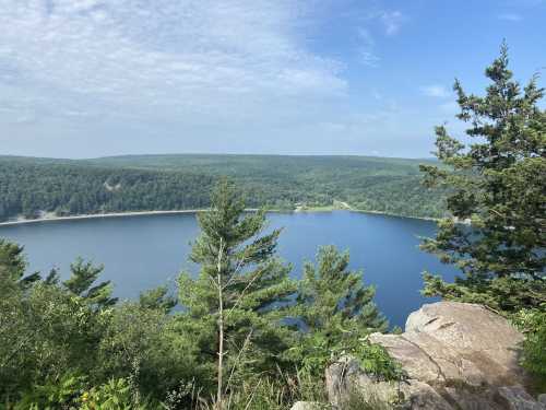 A serene lake surrounded by lush green trees and rocky terrain under a clear blue sky.