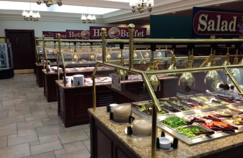 A spacious buffet area featuring multiple food stations with salad and hot dishes, surrounded by elegant decor.