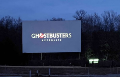 A dark outdoor scene featuring a large billboard displaying the "Ghostbusters: Afterlife" logo.