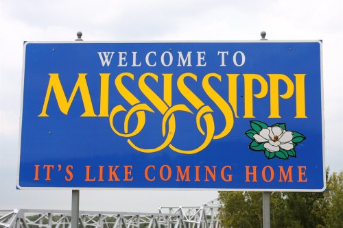 Welcome sign for Mississippi featuring a magnolia flower and the phrase "It's like coming home."