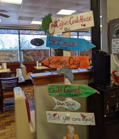 Wooden directional sign with arrows pointing to various locations: Cajun Crab House, St. Louis, Kansas City, Gulf Coast, Downtown.
