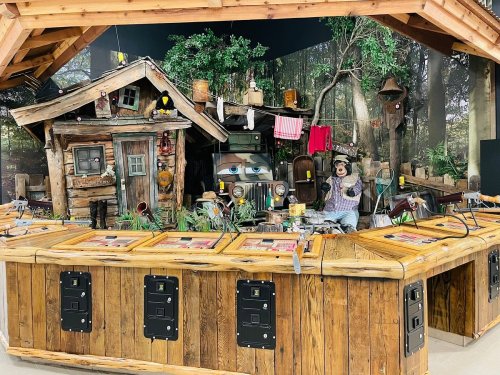 A rustic wooden counter with interactive displays, surrounded by a whimsical forest-themed backdrop and a small cabin.