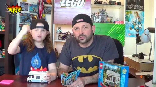 A man and a child sit at a table with LEGO sets, discussing a build while wearing casual clothing and hats.