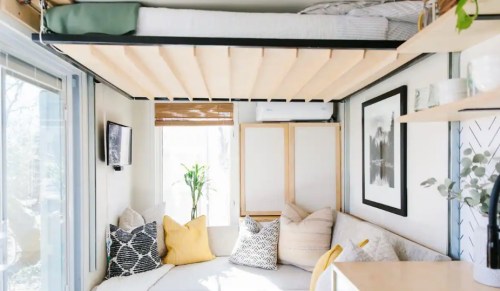 Cozy, modern interior of a small space with a lofted bed, seating area, and natural light from large windows.