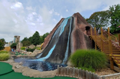 A large artificial mountain with a waterfall, surrounded by greenery and a mini-golf course.