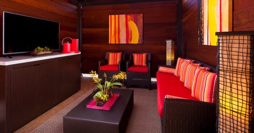 Cozy lounge area with red and black furniture, a TV, and vibrant artwork on wooden walls.
