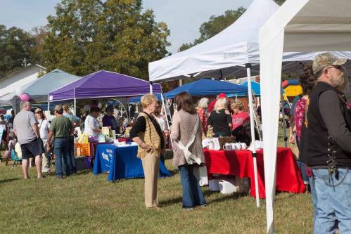 A lively outdoor market scene with people browsing colorful tents and tables under a clear blue sky.