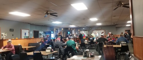 A cozy diner interior with patrons dining, a counter in the background, and autumn decorations on the walls.