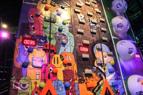 Colorful climbing wall with animated characters, timers, and various holds for climbing. Brightly lit and playful design.