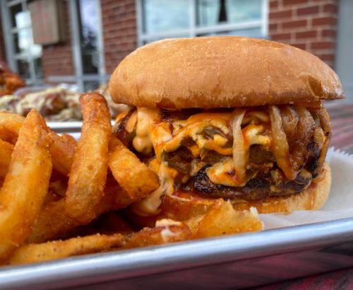 A close-up of a juicy burger with melted cheese and grilled onions, served with crispy fries on the side.