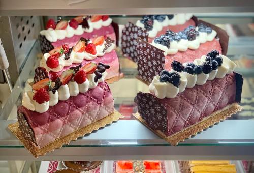 Colorful layered cakes with whipped cream, strawberries, and blueberries displayed in a glass case.