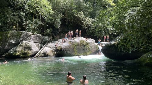 People swimming and relaxing in a natural pool surrounded by large rocks and lush greenery.