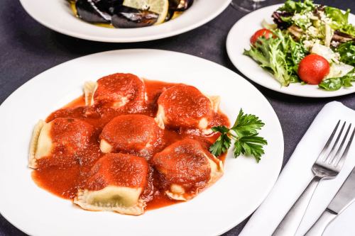 A plate of ravioli topped with marinara sauce, garnished with parsley, alongside a fresh salad.