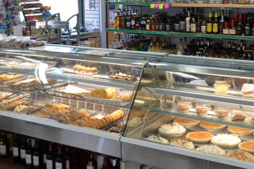 A display case filled with various baked goods and desserts, with shelves of drinks in the background.