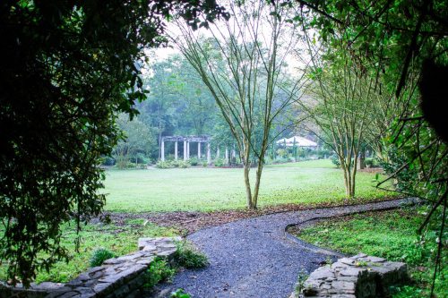 A winding path leads through lush greenery to a serene garden with columns in the background.
