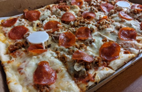A pizza topped with pepperoni, sausage, and melted cheese, served in a cardboard box with white pizza savers.