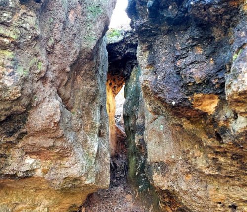 Narrow passage between two large, textured rock formations, with light visible at the end.