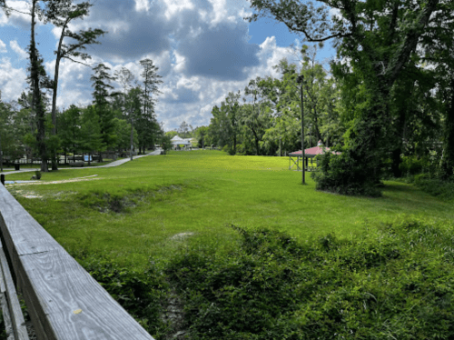 A lush green park with trees, a pathway, and a pavilion under a partly cloudy sky.