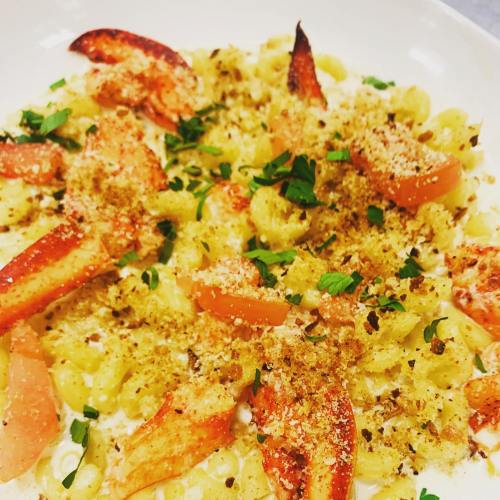 Creamy pasta dish topped with lobster pieces, breadcrumbs, and fresh herbs, served in a white bowl.