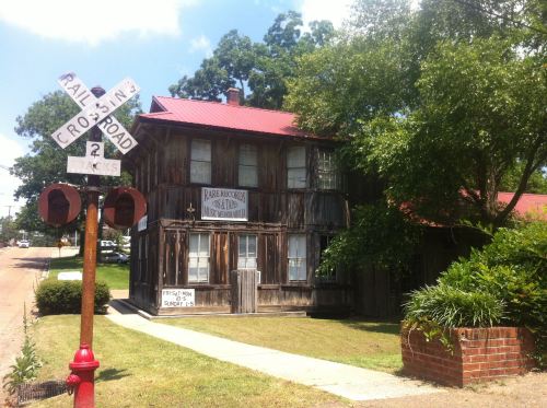 A rustic wooden building with a red roof, next to a railroad crossing sign and surrounded by trees.