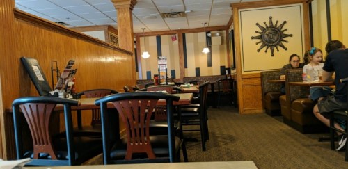 A cozy restaurant interior with wooden accents, tables, and booths, featuring a sun decoration on the wall.
