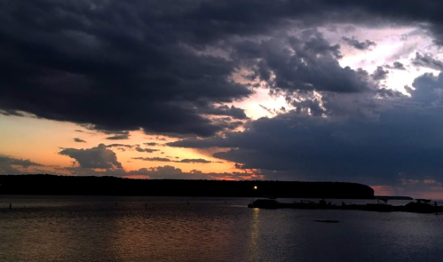 A serene sunset over a calm lake, with dark clouds and hints of orange and purple in the sky.