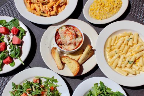 A spread of various dishes including pasta, salad, corn, and baked lasagna on a table.