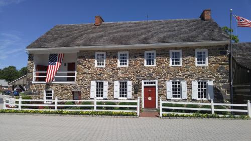 Historic stone building with a red door, white windows, and an American flag, surrounded by a white fence and flowers.