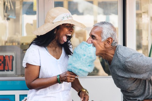 A man and woman playfully compete to eat cotton candy, both laughing and enjoying a fun moment together.