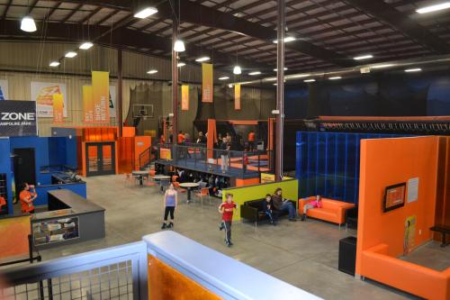 A vibrant indoor trampoline park with colorful walls, people jumping, and seating areas for visitors.
