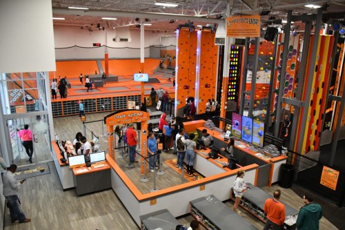 A vibrant indoor activity center with climbing walls, trampolines, and people enjoying various activities.