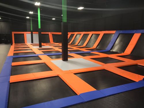 A spacious indoor trampoline park with orange and blue safety pads and multiple trampolines arranged in a grid pattern.