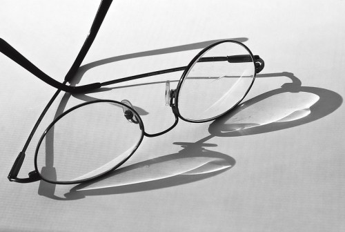 A pair of round black glasses resting on a white surface, casting soft shadows.