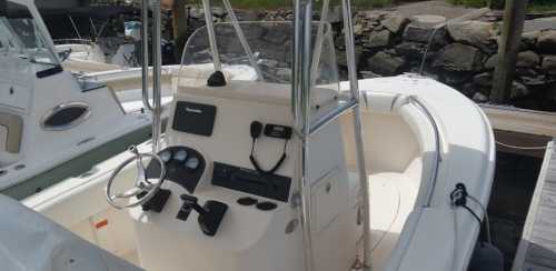 A white boat's cockpit with a steering wheel and dashboard, docked near rocky shorelines.