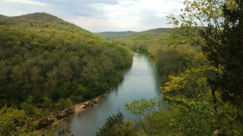A serene river winding through lush green hills under a cloudy sky.