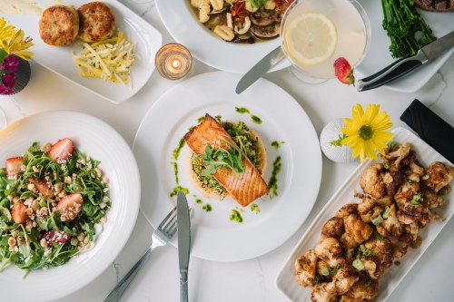 A beautifully arranged table with various dishes, including salmon, salads, and appetizers, garnished with flowers.