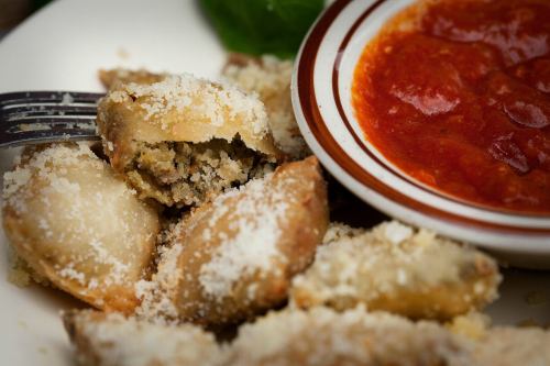 A plate of crispy fried dumplings sprinkled with cheese, served with a side of marinara sauce.