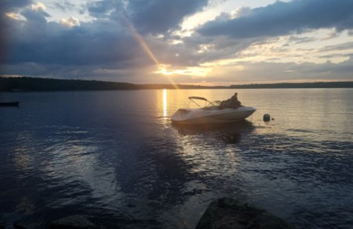A boat on calm water at sunset, with golden rays reflecting on the surface and clouds in the sky.