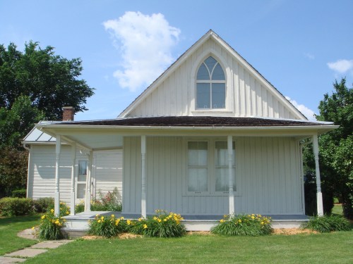 A white, gabled house with a front porch and yellow flowers in the garden, set against a blue sky with clouds.