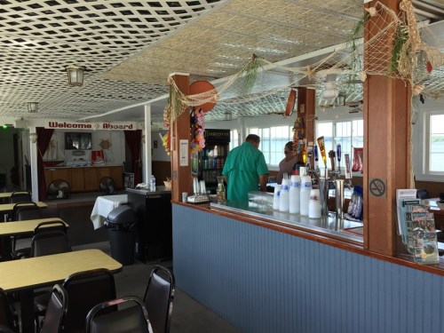 Interior of a casual dining area with tables, a counter, and a welcoming sign, featuring a nautical theme.