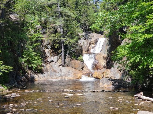 A serene waterfall cascading down rocky terrain, surrounded by lush green trees and a calm river below.