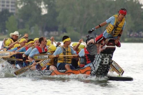 A team of dragon boat racers paddles vigorously, with one member standing on the dragon's head, in a lively competition.