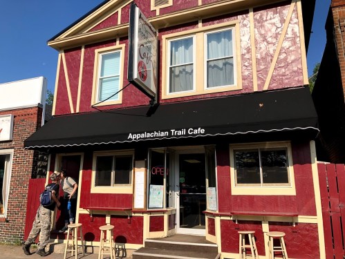 A red and yellow café building with an awning labeled "Appalachian Trail Café" and a person entering.