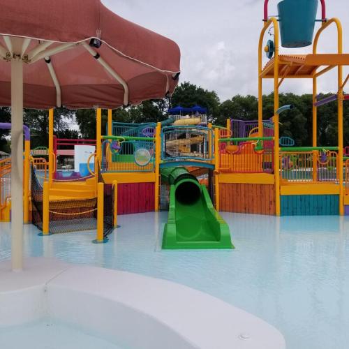 A colorful water park with slides, play structures, and a shaded area under an umbrella.