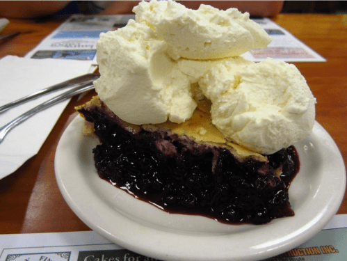 A slice of blueberry pie topped with a generous scoop of whipped cream on a white plate.