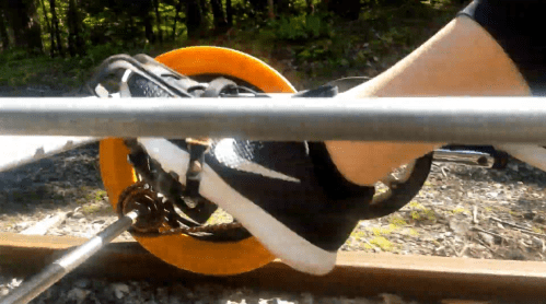 A close-up of a foot in a black sneaker pedaling on a bike-like mechanism on a railway track.