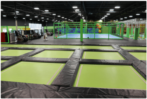 Indoor trampoline park featuring multiple trampolines and a colorful play area in the background.
